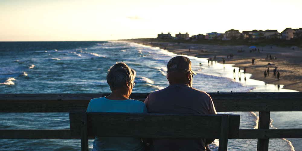 a couple sitting on a bench watching waves roll in to the shoreline