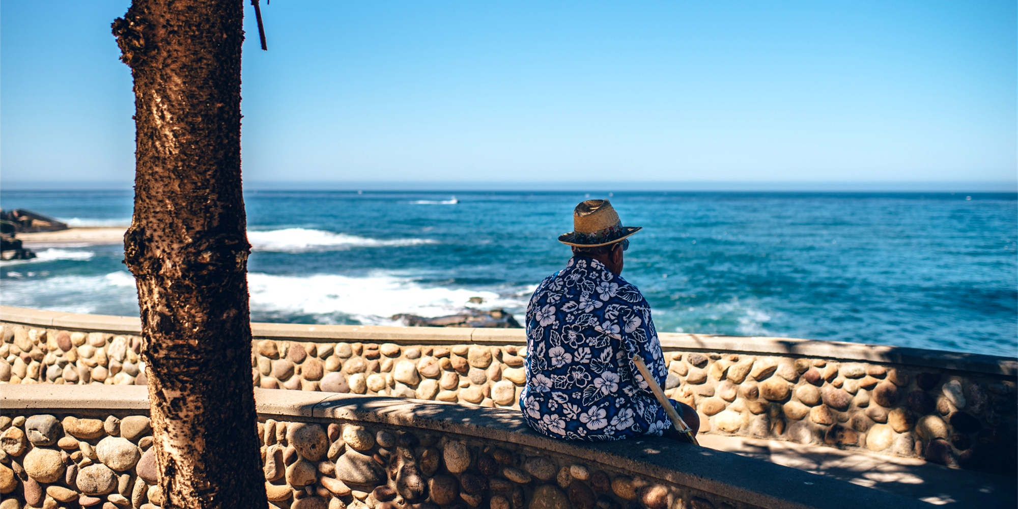 man in Hawaiian shirt sitting near the ocean