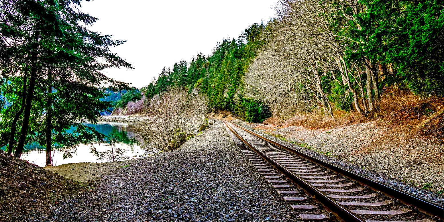 railroad tracks curved around a lake surrounded by a forest